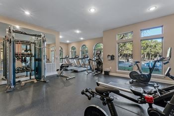A spacious gym with a variety of exercise equipment and a view of the outdoors through large windows.